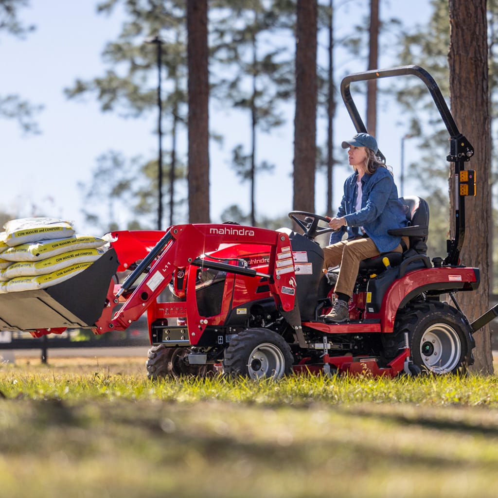 Tracteur sous-compact Mahindra 1120 avec femme transportant une poche de moulée