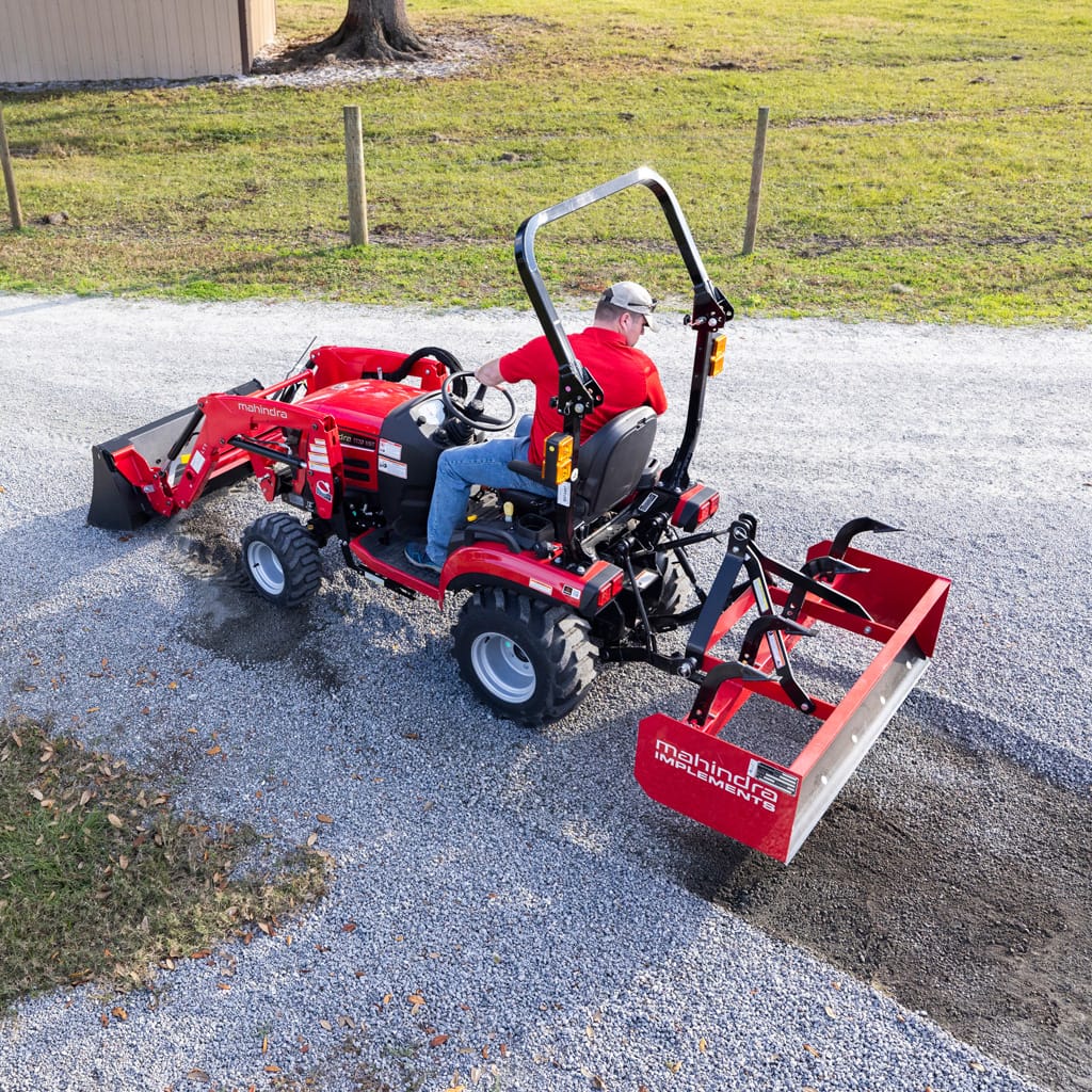 Tracteur Mahindra 1120 sous-compact utilisé avec un box scraper par un homme