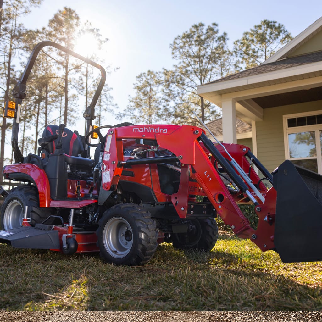 Mahindra 1120 tracteur sous-compact avec tondeuse ventrale et chargeur frontal devant une maison